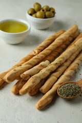 Grissini, olives, oil and spoon with spices on white textured background