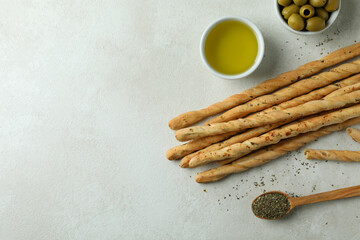 Grissini, olives, oil and spoon with spices on white textured background