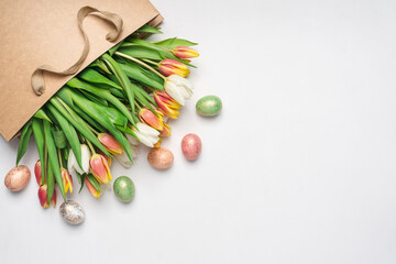 Flowers in craft paper bag and decorative easter eggs on white background. Bouquet of fresh tulips