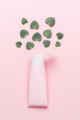 Pink tube with open lid and eucalyptus leaves on pastel pink background. Natural organic cosmetics concept