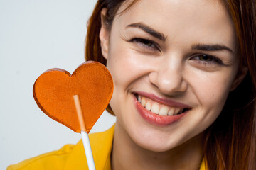 cheerful pretty woman licking heart-shaped lollipop close-up studio