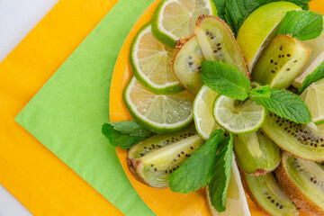 Fototapeta na wymiar beautiful slicing of juicy fresh fruits - lime, kiwi, decorated with a sprig of mint on a yellow and green napkin