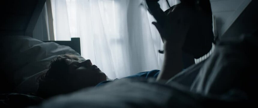 Cute little Caucasian kid boy lying on bed, playing baseball catch with himself at home. Shot with 2x anamorphic lens