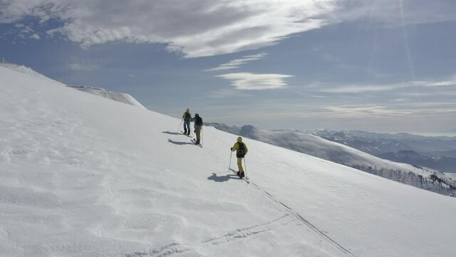 Drone shot of three persons on splitboards climbing mountain.