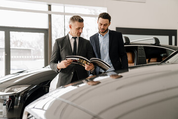 Mid unshaven manager working with mature customer in car showroom