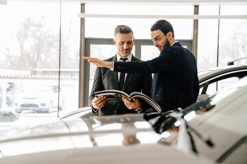 Mid unshaven manager working with mature customer in car showroom