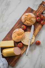 Feine Leberwurst aus Kalb und Schwein mit Weizen Rosen Brötchen, Tomaten, Butter und Messer auf Holzbrett, Geschirrtuch und Marmor Hintergrund als Frühstück
