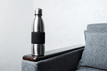Close-up of steel reusable thermo water bottle on sofa, against grey wall.