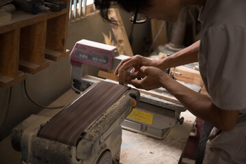 Carpenter polishes a wooden parts on a grinding machine. Close-up hands.