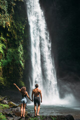 Fototapeta na wymiar Couple at the waterfall, rear view. Couple on vacation in Bali. Honeymoon trip. A couple in love travels the world. Vacation on the island of Bali. Tourists in Bali. Copy space