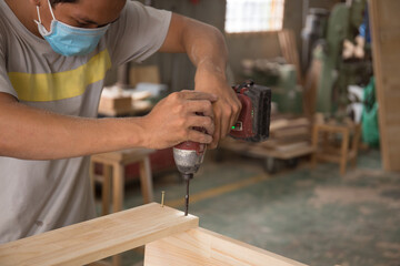 Close-up of carpenter using electric drill in workshop and routing out holes Cabinetmaker drilling wood on table. Joinery work on the production and renovation of wooden furniture. Small Business