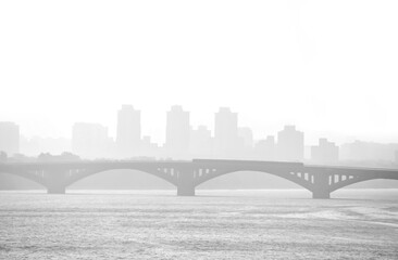 Fototapeta premium Train traveling on the bridge over the river Dnipro foggy morning. Bridge over river in misty morning. Kiev skyline silhouette. The Metro bridge in Kiev with fog and silhouette of city in background.