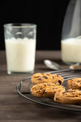 Close-up of cookies on wire rack, wooden table with glass and bottle of milk, selective focus, black background, vertical