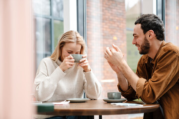 Young man and woman smiling and talking while drinking coffee in cafe