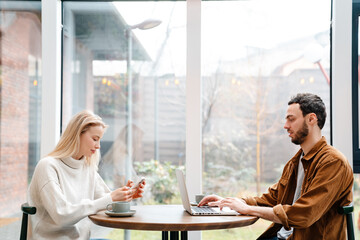Focused man and woman using laptop and cellphone while drinking coffee