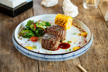 Grilled fillet mignon steaks with corn and salad on the wooden table