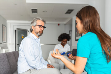 Fototapeta premium Doctor consulting patient in hospital waiting room. Patient sitting . Diagnostic, prevention of diseases, healthcare, medical service, consultation or education, healthy lifestyle concept