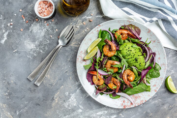 Green salad with avocado and shrimps salad. Seafood concept. Tasty veg mixed leaves, grilled prawn shrimps. Delicious breakfast or snack on a gray background, top view