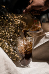 Barista pouring milk into a glass of iced coffee