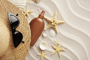 beach accessories - suntan lotion, sunglasses and summer hat on sand beach background