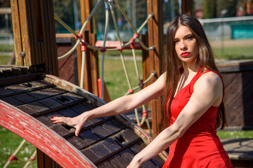 Young girl in red short dress in a public park, standing on park playground