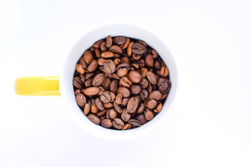 Cup filled with roasted coffee beans isolated on white background, top view. Copy space for text. Selective focus.