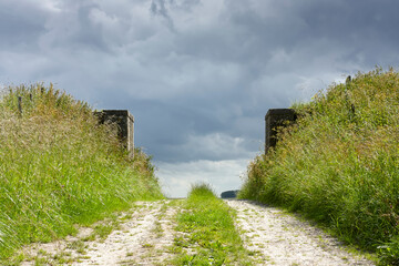 Old brick gate in a dike overgrown with saturated green grass under a dark stormy sky. Concept of...
