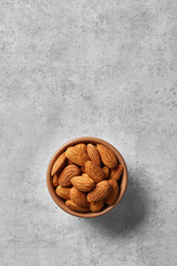 Almonds in a bowl viewed from above on a grey background. Top view. Copy space