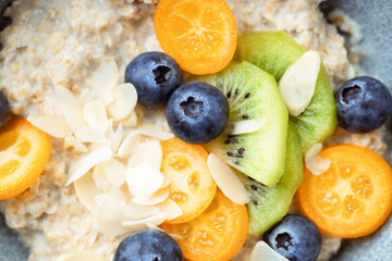 Close up of oatmeal porridge with kumquat, blueberries, kiwi and almond flakes in a bowl.