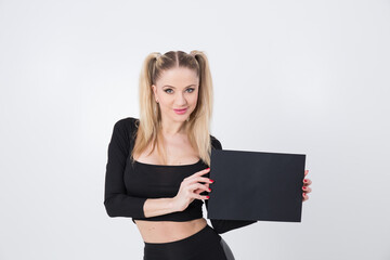 A beautiful blonde in black clothes holds a sheet of black paper in her hands. 