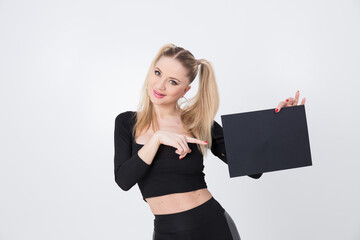 A beautiful blonde in black clothes holds a sheet of black paper in her hands. 