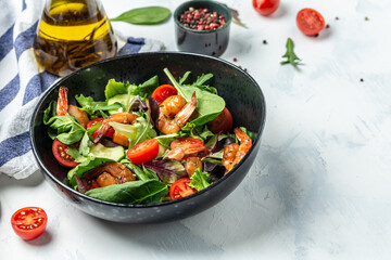 Green salad with smoked shrimps, cherry tomatoes, cucumber and mixed leaves. Seafood concept. Delicious breakfast or snack on a light background, top view