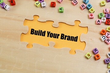 Build Your Brand written on the yellow background with missing puzzle and small alphabets cubes scattered 