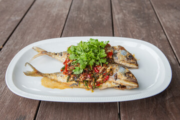 Mackerel with chili sauce in a white tiled plate on a wooden table.