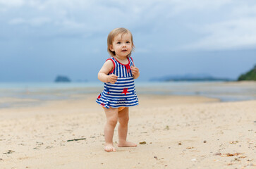 Toddler baby doing her first steps on sand near the bank. Little cute girl playing on the beach. Small child enjoying vacation by the sea or ocean. Travelling with kids concept. Photo with copy space