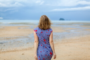 Attractive and happy middle aged woman walking along the seashore on misty day. Mature female joyful expression, recreation leisure. Joyful woman enjoying the freedom of the beach. Copy space