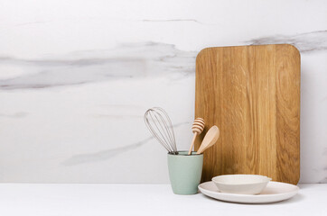 Blank wooden board, plates, cup and utensils in it on the white kitchen table.Empty space