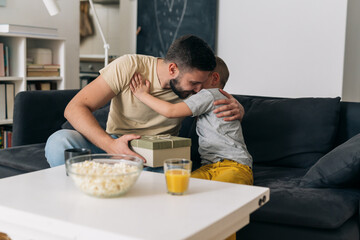 father and son sharing presents. they are sitting in the living room