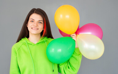 Fototapeta na wymiar A beautiful young joyful girl holding a bunch of colorful balloons on a gray background. Bachelor party's party holiday concept.