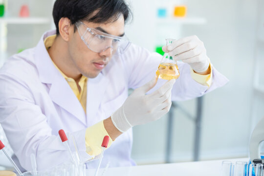 Close up hand. Asian scientist holds a scientific liquid in a beaker. protective equipment protective clothing, goggles, gloves inside the scientific laboratory. Concept medical coronavirus covid19.