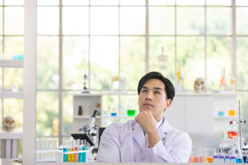 Asian man scientist or researcher sitting wearing white coat and serious face thinking about...
