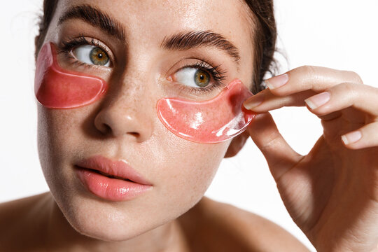 Under eye masks for puffiness, wrinkles, dark circles. Eye patches concept. Satisfied woman naked, applying pink eye patches in bathroom while looking at the mirror