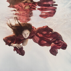 A girl in a fluttering red dress swims underwater as if flying in zero gravity