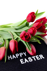 Felt board with message "Happy Easter" with fresh red tulips bouquet, closeup