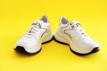 white sports sneakers with black soles on a yellow background