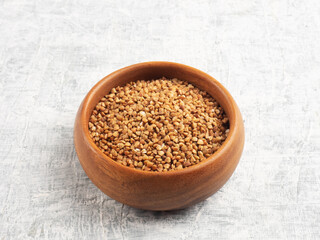 Buckwheat in a wooden cup on a white concrete background