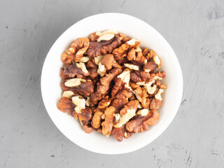 Shelled walnuts in ceramic bowl on gray concrete background