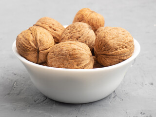 Walnuts in a white bowl on gray concrete background