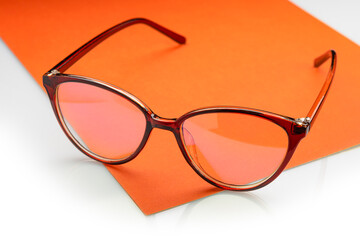 Glasses in a plastic frame with transparent lenses, on an orange sheet of paper