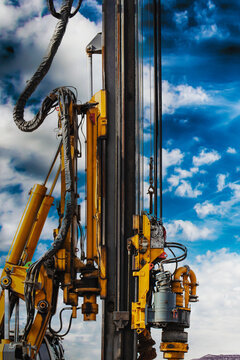 Hydraulic drilling rig against the blue cloudy sky. Vertical image. Installation of bored piles by drilling. Foundations and foundations. Drilling in the ground.